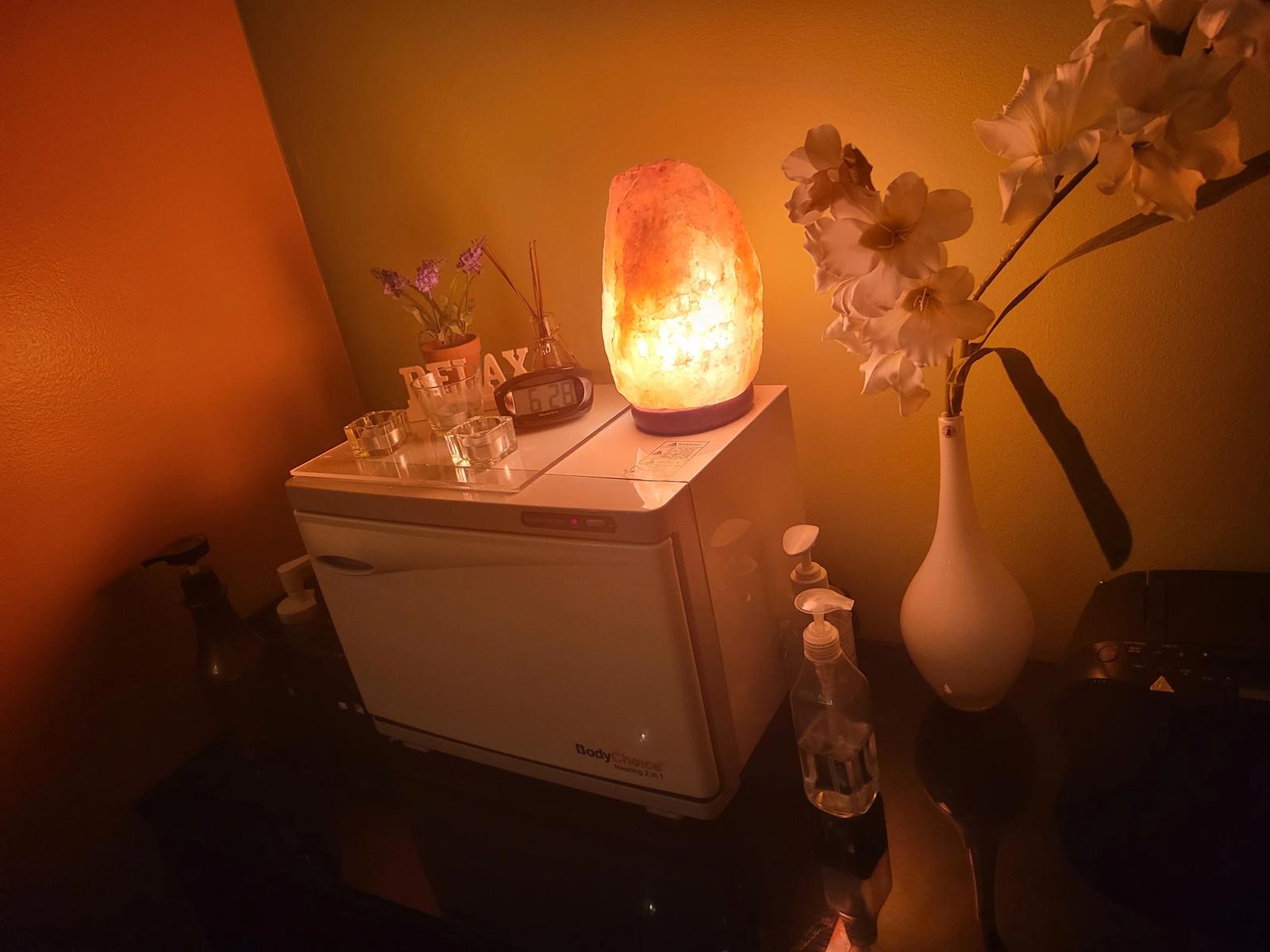 A treatment room at Sunrise lit by a warm salt lamp, with a towel warmer and fresh flowers